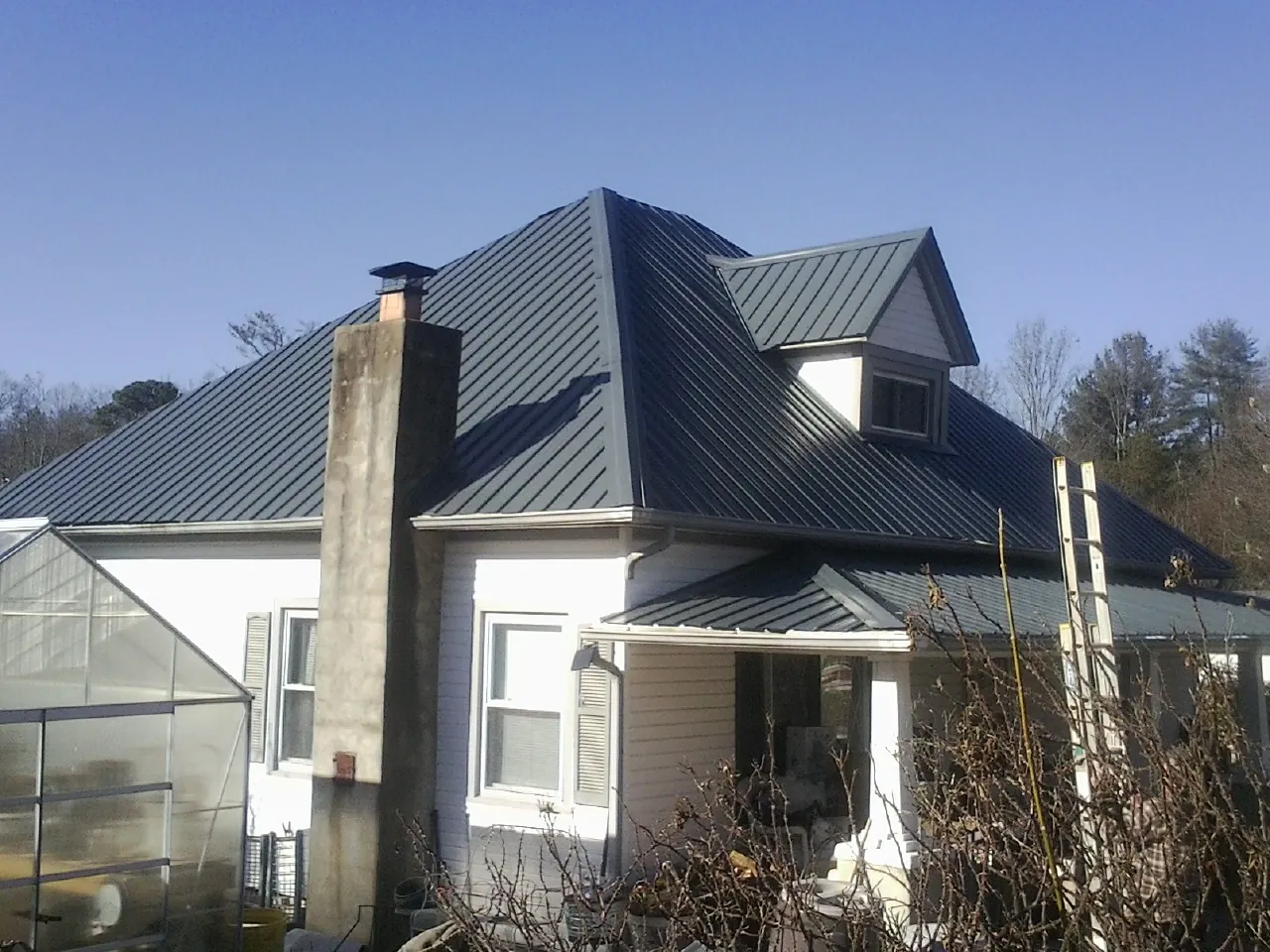 Dark blue standing seam metal roof on a white farmhouse with dormer — Slate & Tile Roof Repair by Roofing Brothers in Gladstone