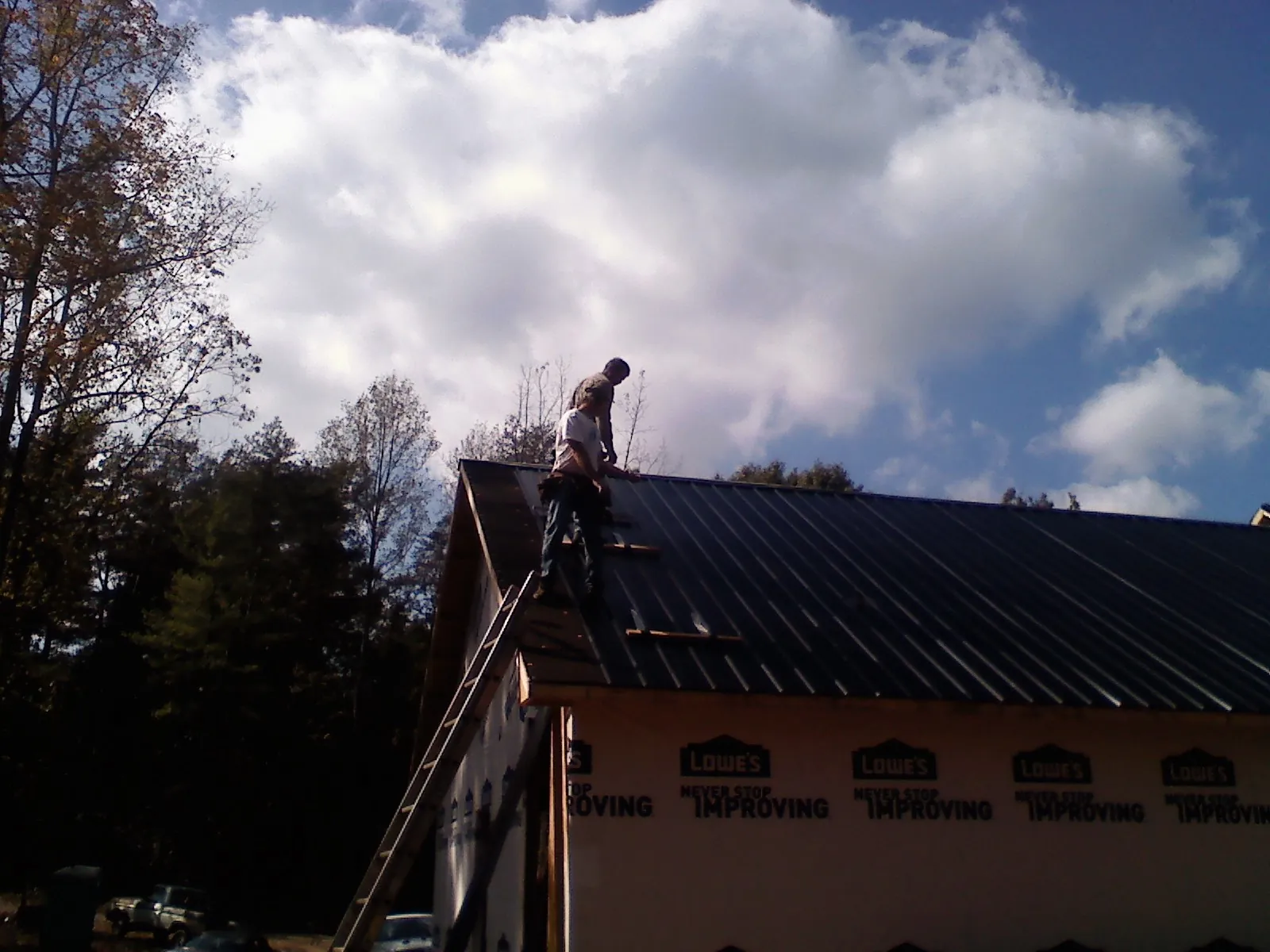 Roofer fastening dark metal panels high against a cloudy sky, from a Roof Inspection job in Gladstone